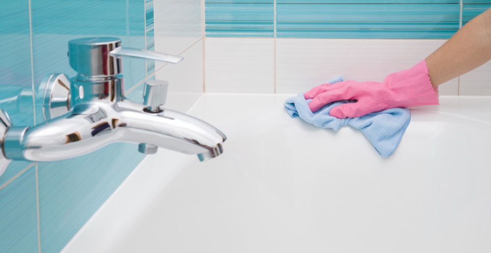 Wie wirkt Entkalker? Hand mit Putzlappen wischt über Badewanne, saubere Armatur ohne Kalk